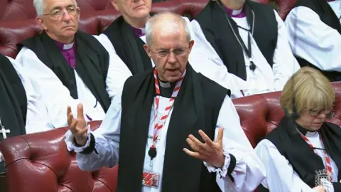 UK Parliament/PA Justin Welby delivers a speech with his hands splayed against a backdrop of the red benches in the House of Lords