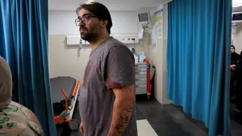 A Palestinian father stands in a Hebron hospital emergency room with his clothes stained with blood. His his seven-month-old baby was killed by Israeli forces, the Palestinian health ministry said. Photo: 5 June 2026