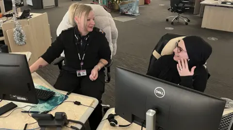 Two female call operators sat at their desks in front of multiple screens