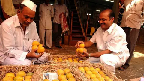 Getty Images the image offers an offer for merchants and buyers for Alphonso Mango, and wearing traditional hats in a market in Mumbai, Maharashtra, India. 