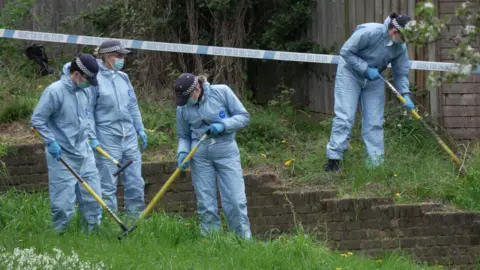 PA Media Police officers wearing blue overalls searching grassland