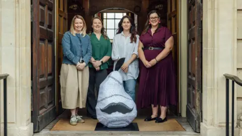 Worcester BID A group of four women stand in front of a blue sculpture of a pear with a black moustache on it.