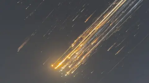 Reuters Orange balls of light as SpaceX rocket debris flies across the sky from top right to bottom left