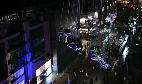 AFP via Getty Images People on an aerial ride looking down on the street below