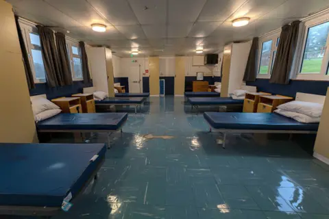 Home Office via PA Media A dormitary containing multiple beds in a room with white ceiling and blue floor.