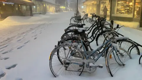 Sepeda Maddy Savage yang tertutup salju berdiri di jalan perbelanjaan yang hampir sepi di Skellefteå.