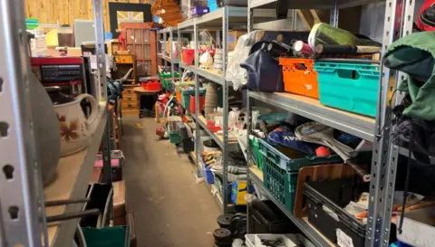 An aisle of various items stacked on shelves and boxes inside the shop