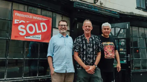 Lee London / MVT Three men, Peter Cornforth, Norman Cook, and Thomas Evrenos outside The Pipeline.