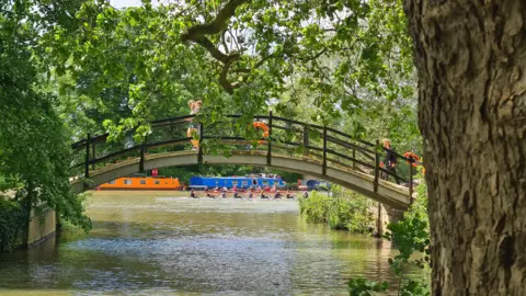 Rebekah TUESDAY - Two people walk over a bridge over the Thames as a crew of rowers pass underneath