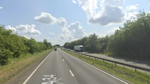 Google A screenshot from Google street view showing a dual carriageway with a central reservation and barrier in the middle, with trees on either side, on a sunny way.