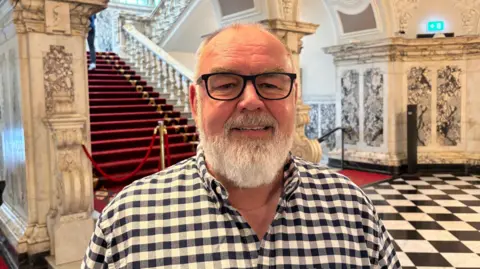 Eric Hanvey. He has a white beard, wearing glasses and a black and white gingham shirt.