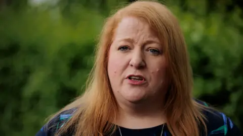 PA Naomi Long, pictured at a prior press hearing - she has red hair and a colourful top on 