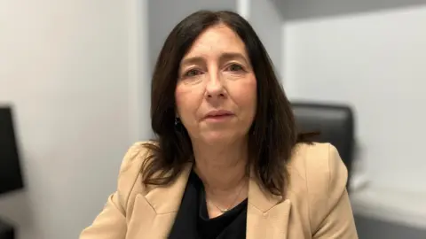 SAM READ/BBC A head and shoulders photo of Theresa Halston who is looking at the camera. The background behind her is blurred out, but she is in an office environment and sitting down on a black office chair. Part of a computer monitor can be seen to the left of the picture. 