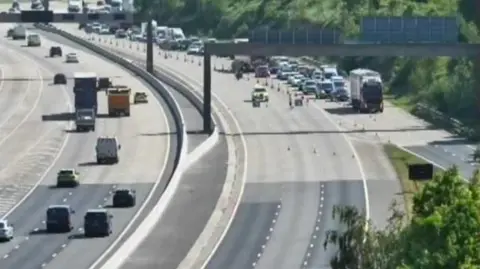 A photo from a traffic camera on the M1 showing police at the scene of a crash and a road closure in place.