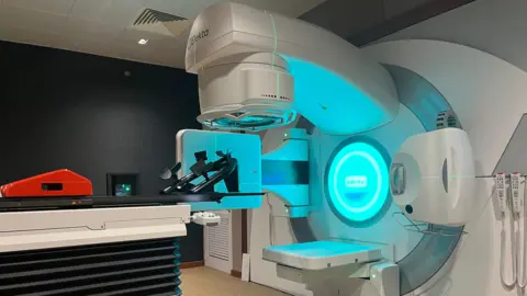 La máquina de radioterapia del hospital se iluminó con una luz azul. Hay una cama en la que los pacientes pueden tumbarse con reposacabezas.