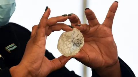 A woman with painted nails holds a large diamond