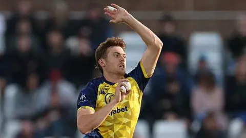 Kasey Aldridge bowling for Durham in the T20 Blast with his right hand holding the white ball and his left hand raised high for leverage