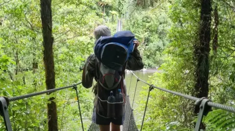 Dougie Haynes Dougie Haynes carrying two golf bags across a metal wire bridge.
