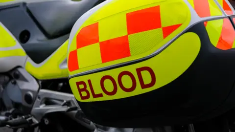 Getty Images A close up of a motorcycle, with a compartment that says blood on it in red lettering. The motorcycle is a blood blike, and is yellow with orange squares on it.