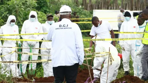 People in white lab coats inside at cordoned-off area at the grave site in Kericho