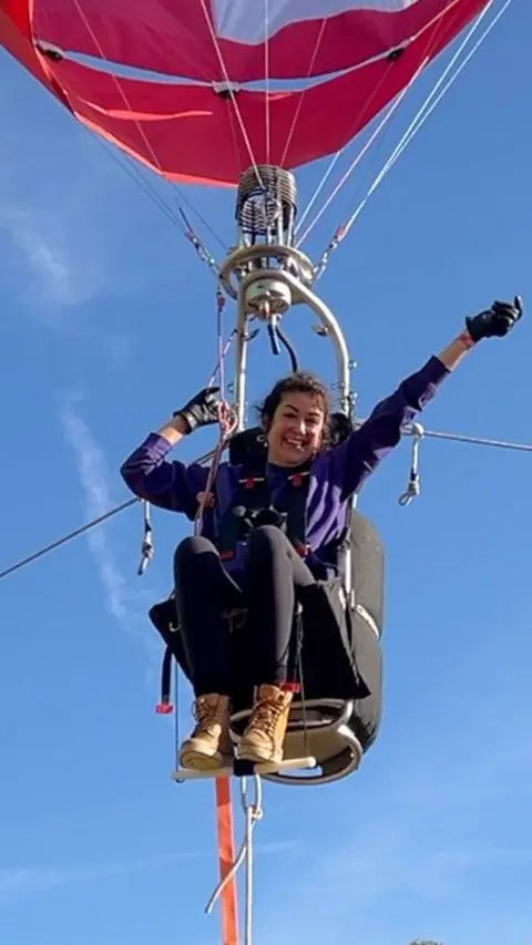 Woman seated below a hot air balloon, celebrating with a hand in the air.