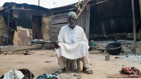 Reuters A man sits in front of the remains of his burnt house at the Woro community.