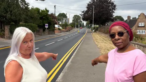 Two women pointing at a road.