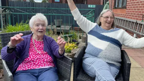 Tom MacDougall/BBC Smiling Margaret Cooper and Joan Giggal raising their hands in the air.