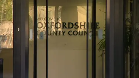 BBC Automatic folding doors at County Hall - the headquarters of Oxfordshire County Council - can be seen closing. Behind them is lettering saying "Welcome to Oxfordshire County Council".