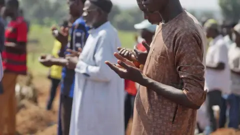 Ifeokbasi Etang/BBC Male Muslim mourners raise their hands in prayer as they attend a funeral at Tudun Wada cemetery. 