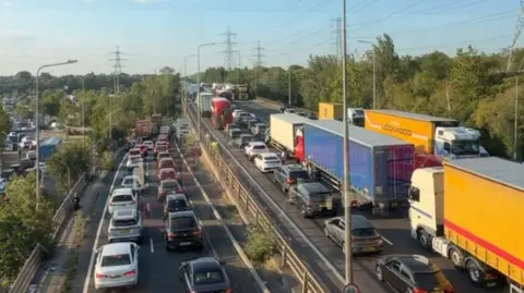 Queues on the M25, its slip road and a local road next to it. There is severe congestion and and no car appears to be moving.