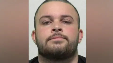 Northumbria Police Mugshot of Roberts. He has a large round head with shaved black hair and a black beard. 