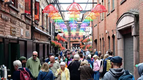 Pacemaker People in the Cathedral Quarter in Belfast under the multi-coloured umbrellas. There are pubs either side.