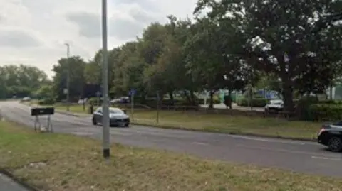 A view of part of Rowley Lane shows cars on a dual carriageway with trees and industrial buildings in the background