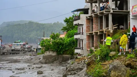 Getty Images Flooding in a village. There are some people standing on top of a building for safety. 