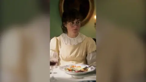 A woman sits at the dinner table wearing glasses