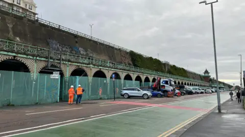 George Carden/BBC Two workers in hi vis stand looking at Madeira Terrace in Brighton, ahead of maintenance work beginning on Monday