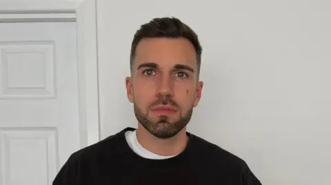 Matthew Connor Matthew Connor with short brown hair and a brown beard wearing a black round neck jumper with a white t shirt underneath