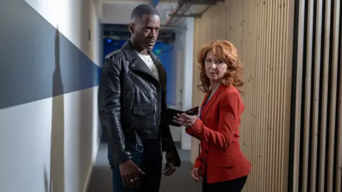 Sophie Mutevelian/Bad Wolf/BBC Studios The Doctor and Mel (Bonnie Langford) appear at S Triad Technology HQ.