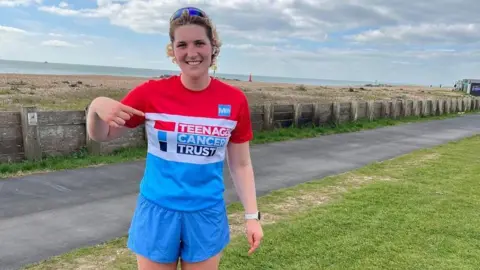 Faye Mullins A woman with blonde hair and sunglasses on her head wearing a red, white and blue Teenage Cancer Trust T-shirt. 