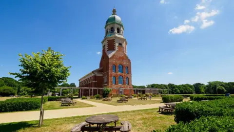 Getty Images A large red brick building with picnic tables, trees and grassy areas.