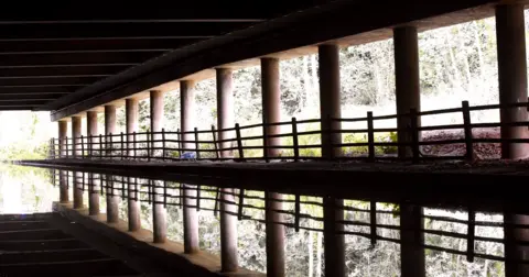Canal reflections of a concrete pillars underneath a road system.