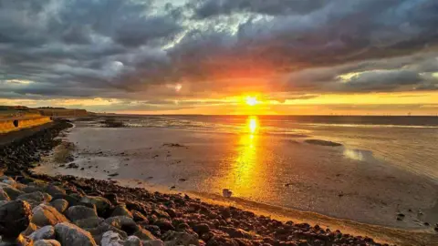 Jane White The sun setting over a beach.