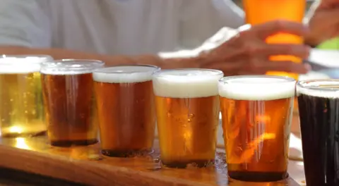 A row of beers with someone in a white tshirt in the background holding a glass of beer.