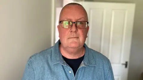 BBC / Simon Spark Stephen Ellis. He is looking at the camera, wearing glasses, a black T-shirt and light blue shirt