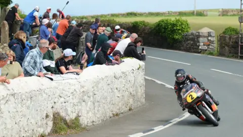 Southern 100 Road Races A motorcyclist going around a corner with spectators watching on behind a wall.