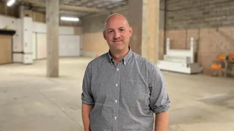 Simon Thake A middle aged man stands in an empty shopping unit with pillars