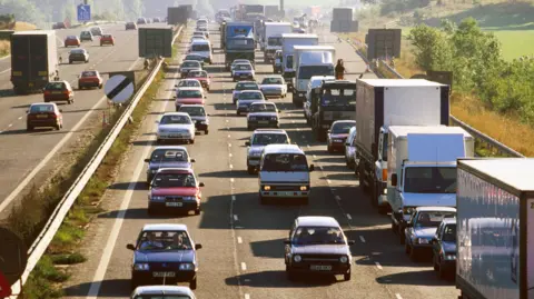 Three lanes of traffic queue on one section of the M25, while traffic continues to flow smoothly on the opposite carriageway.