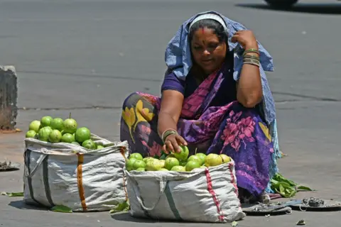 Getty Images A fruit vendor covers her head with a cloth while waiting for customers by a roadside on a hot summer day in Hyderabad on April 25