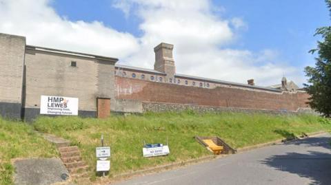 A Google maps image of Lewes Prison with a sign on the exterior of the high brick walled building that reads HMP Lewes